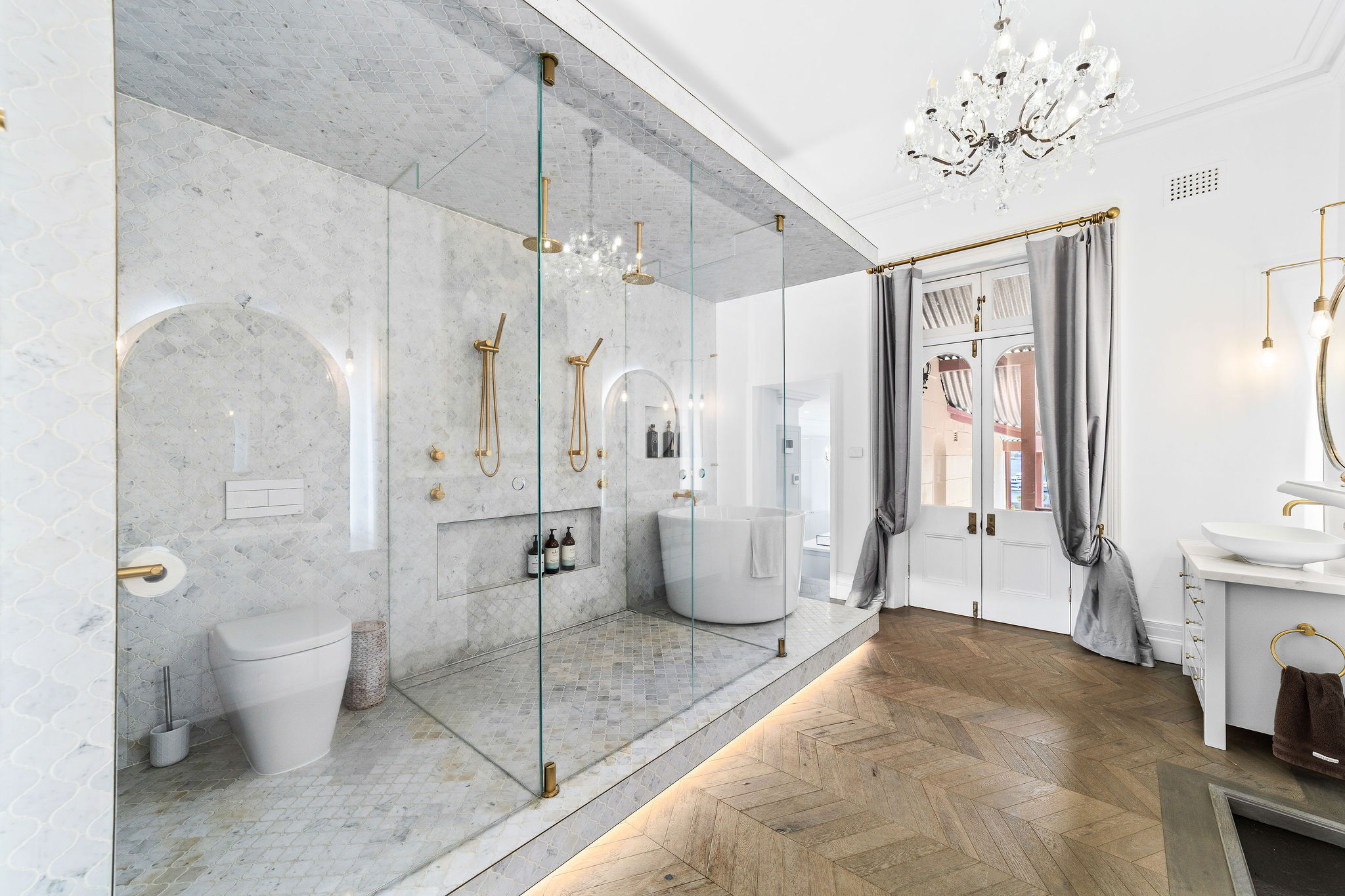 Marble ensuite bathroom with brass fittings, freestanding bath, and crystal chandelier